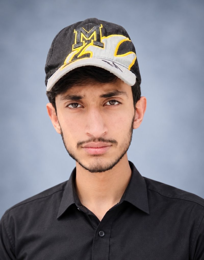 Portrait of Huzaifa Kassar (Huzafig), wearing a black cap and black shirt against a blue studio background